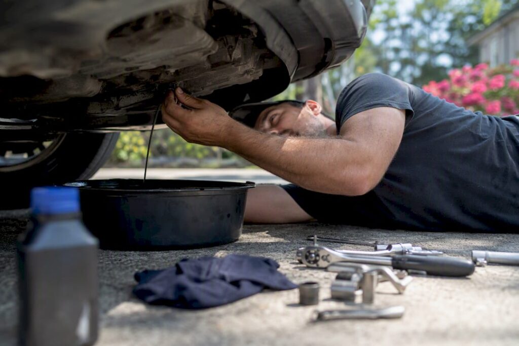 Mechanic draining car oil on driveway